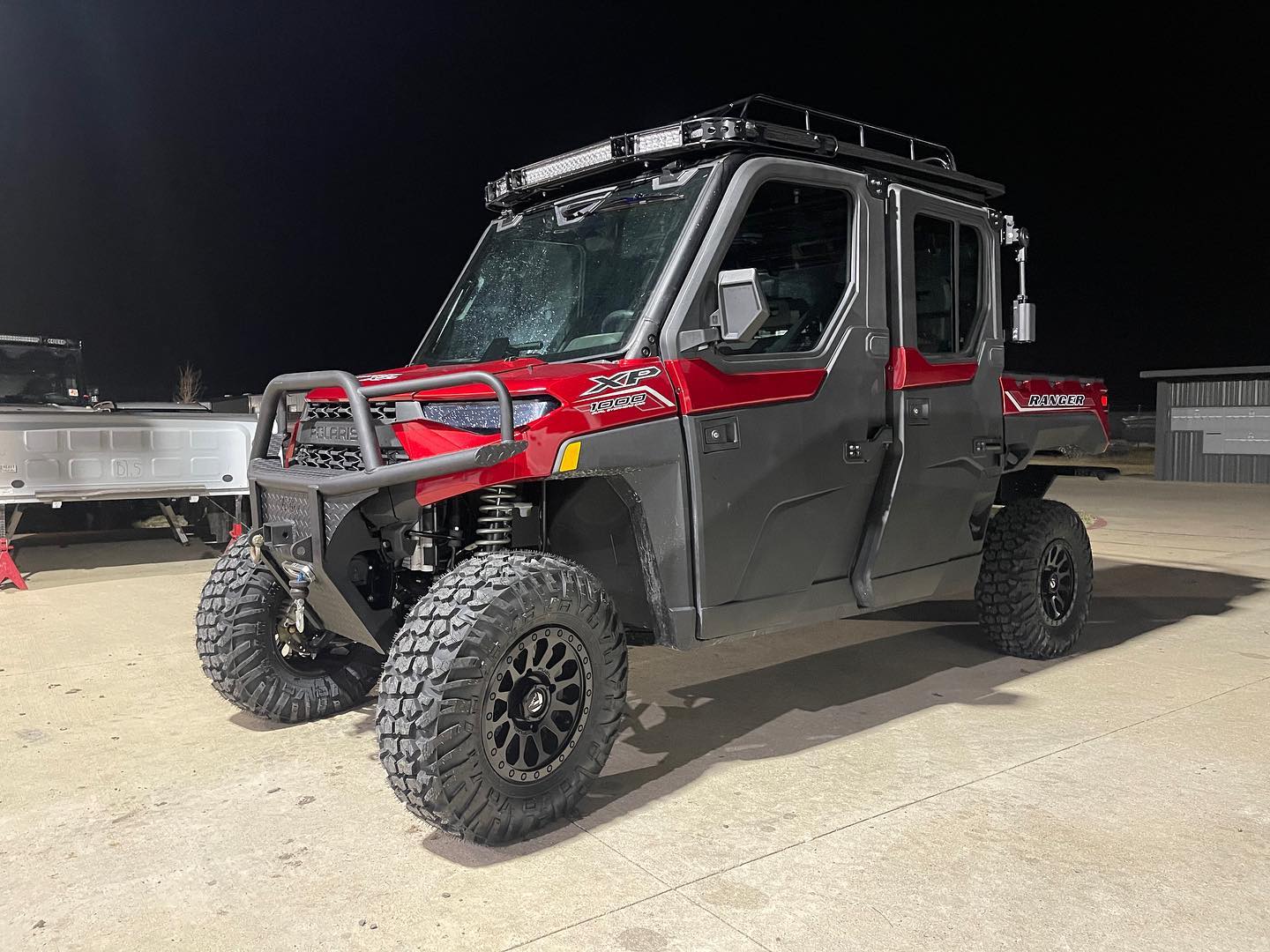 Red Polaris Ranger XP 1000 with full cab enclosure, roof rack with LED light bar, front bumper, and custom wheels