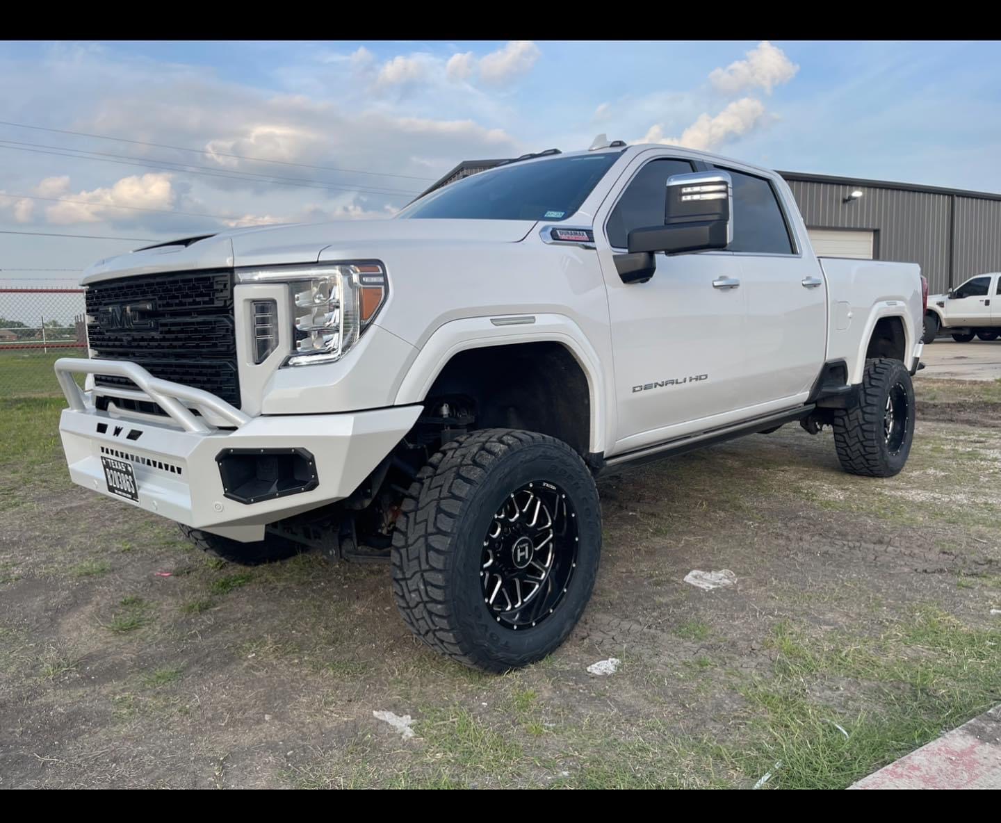 Lifted white GMC Denali HD with custom bumper and aggressive off-road tires